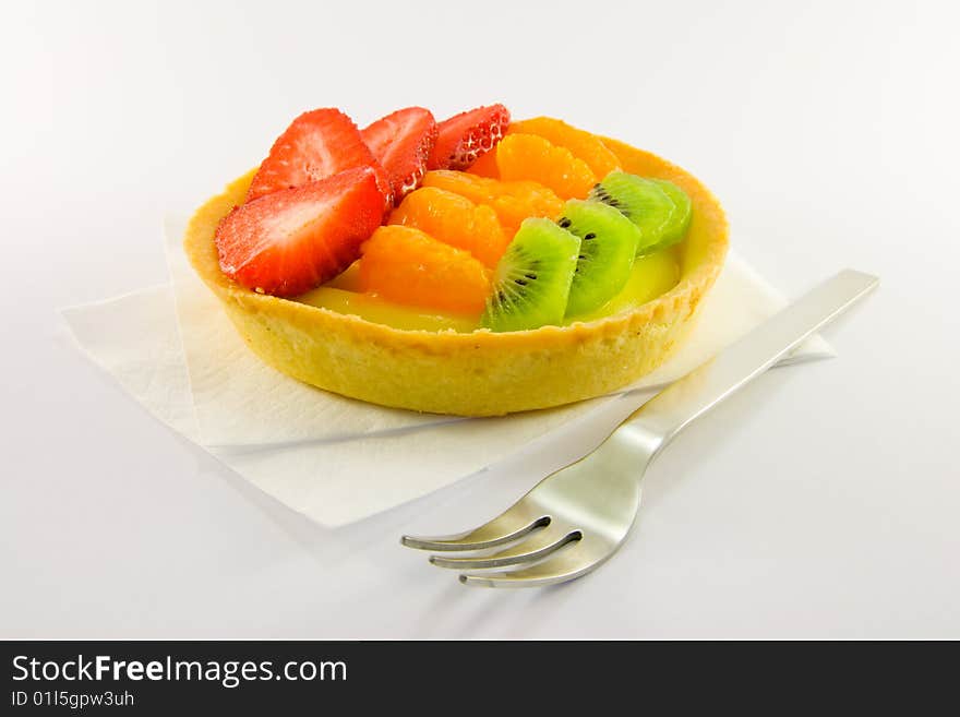 Strawberry, mandarin and kiwi custard fruit tart on a napkin with fork on a  white background. Strawberry, mandarin and kiwi custard fruit tart on a napkin with fork on a  white background