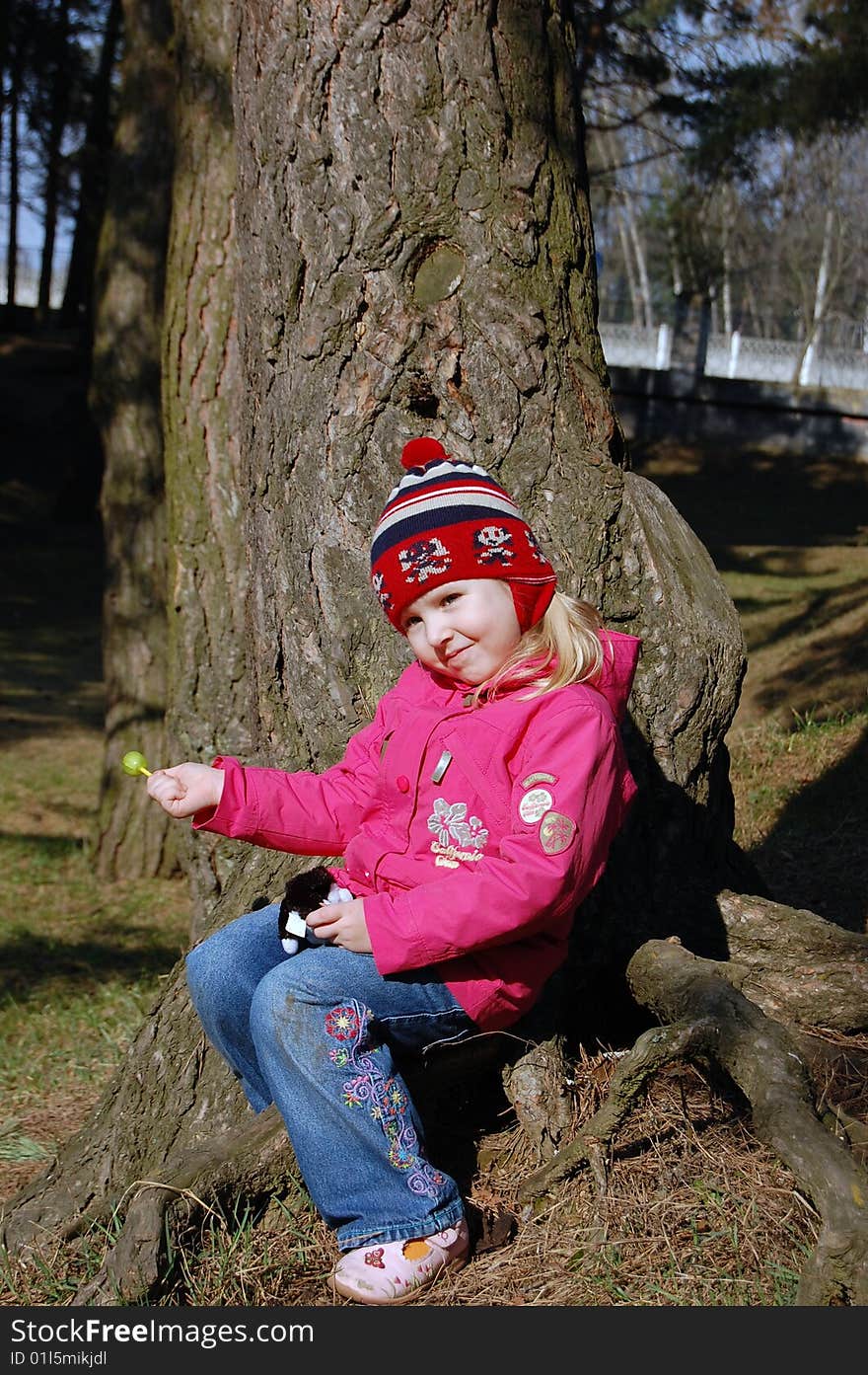 Little girl sit on root in forest eat lollipop. Little girl sit on root in forest eat lollipop