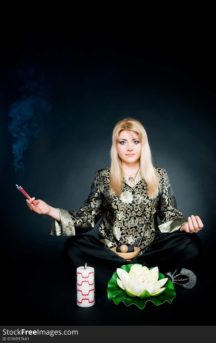 Woman relaxing in lotus pose with aroma sticks, lotus, and candle