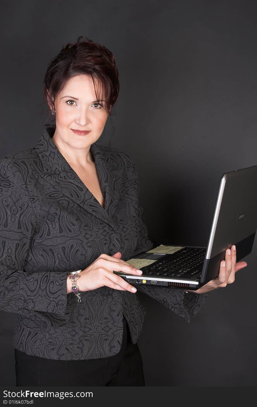 Composed Businesswoman holding a laptop against a black background. Composed Businesswoman holding a laptop against a black background