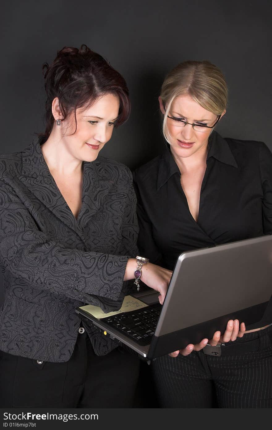 Composed Businesswomen holding a laptop against a black background. Composed Businesswomen holding a laptop against a black background