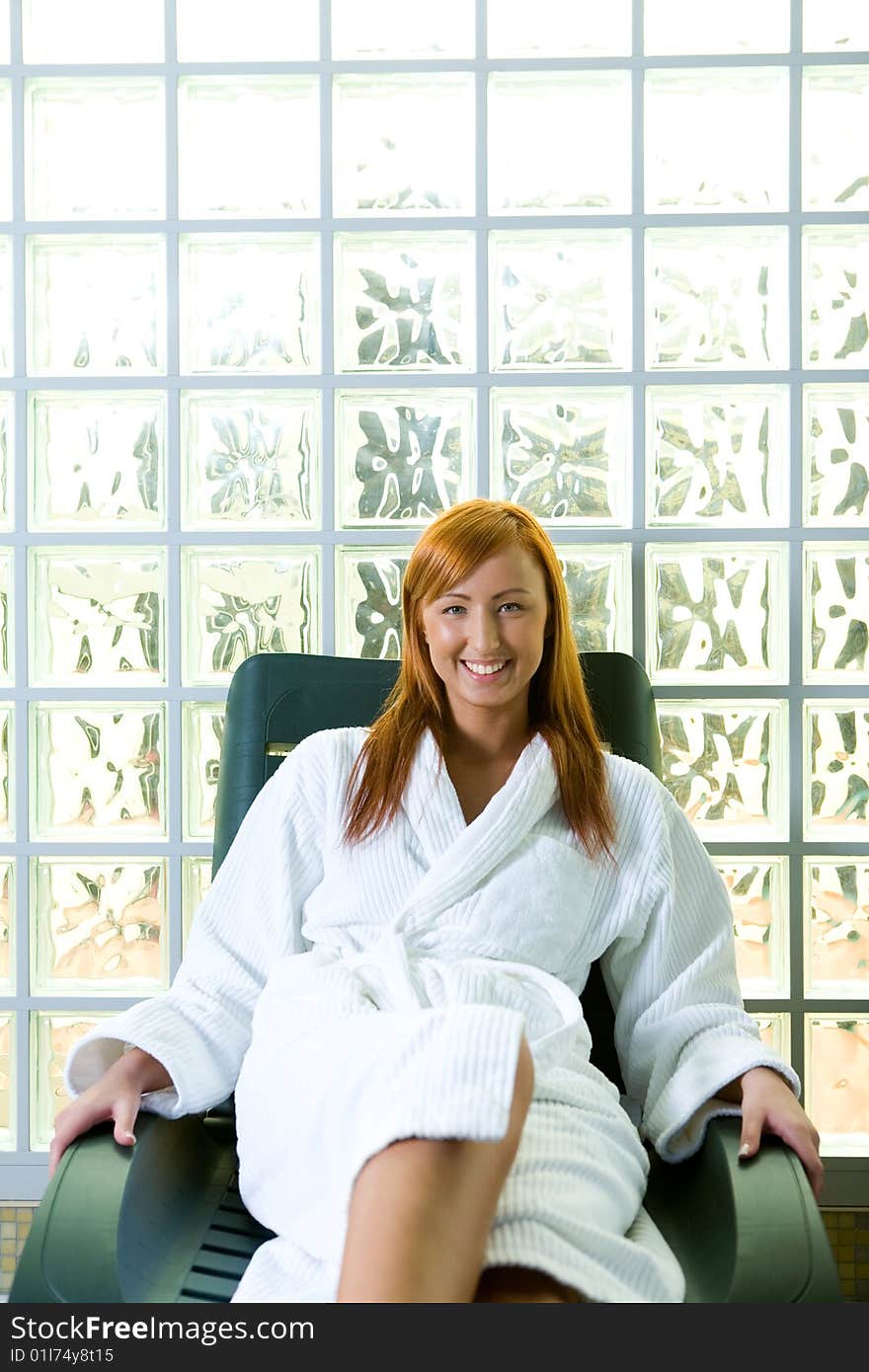 Young red-haired woman clothed bathrobe sitting on deckchair. She's smiling and looking at camera. Front view. Young red-haired woman clothed bathrobe sitting on deckchair. She's smiling and looking at camera. Front view.