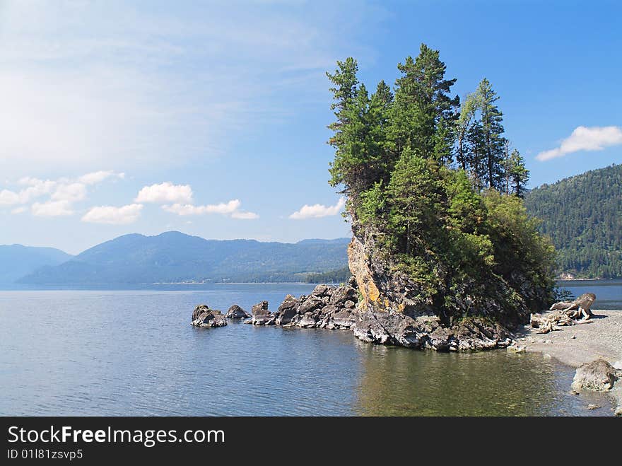 Small rocky cape with trees on mountain lake