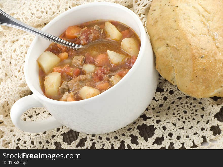 A hearty bowl of homemade beef stew the loaf of bread on a crocheted beige doily