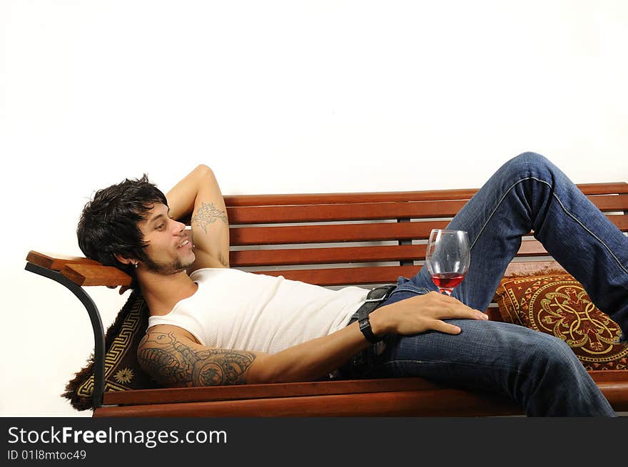 Portrait of a young man reclining over a bench with glass of wine. Portrait of a young man reclining over a bench with glass of wine