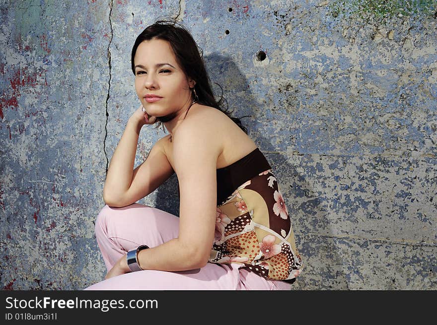 Portrait of young female fashion model sitting against grunge wall