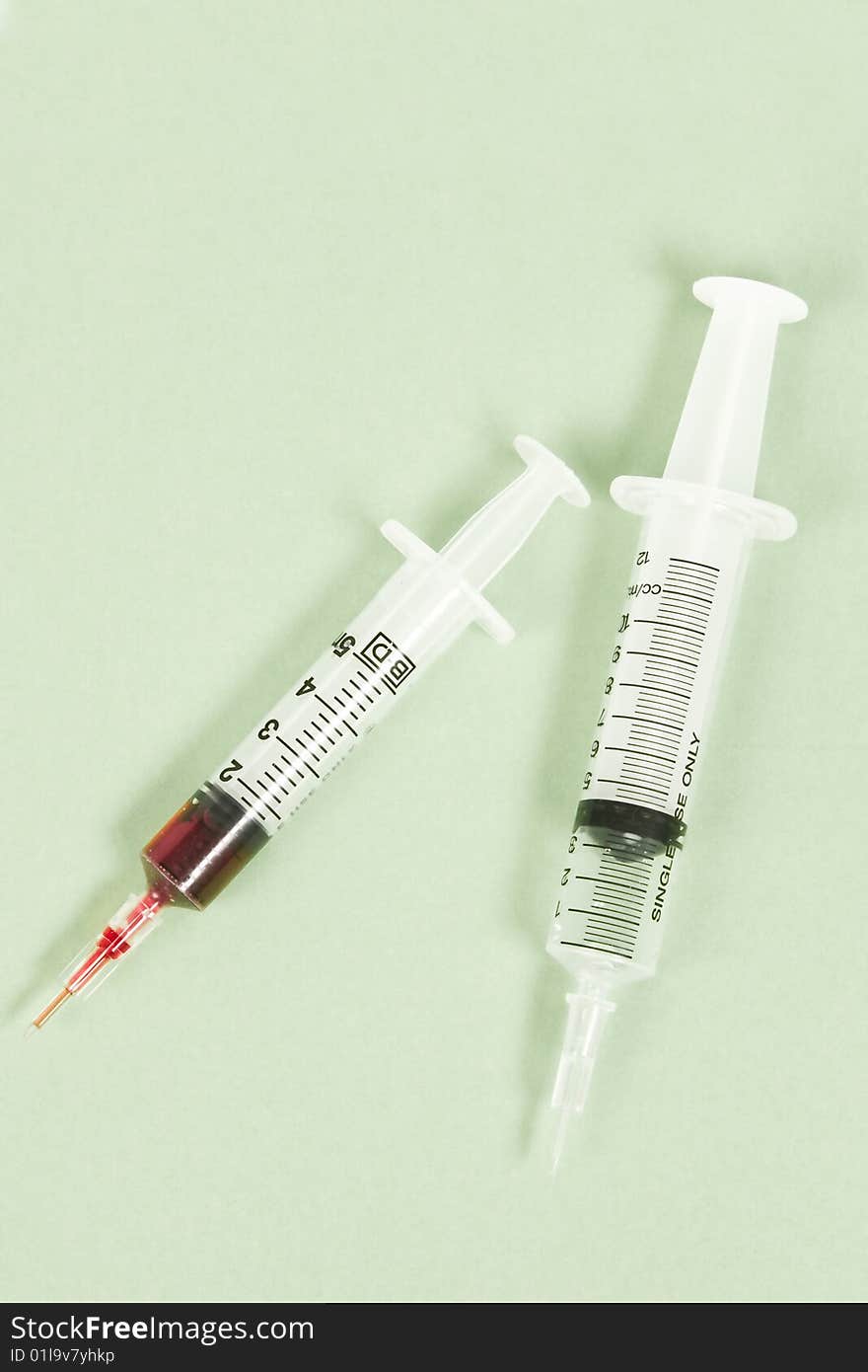 Two syringes on green background, one syringe filled with blood