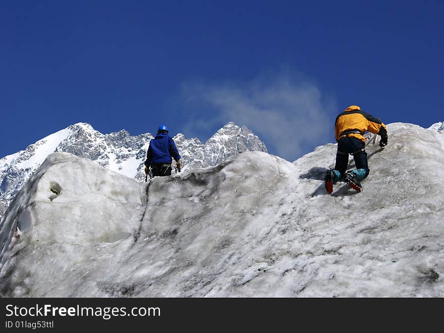 Two climbers practice on an ice wall on a background mountains. Two climbers practice on an ice wall on a background mountains