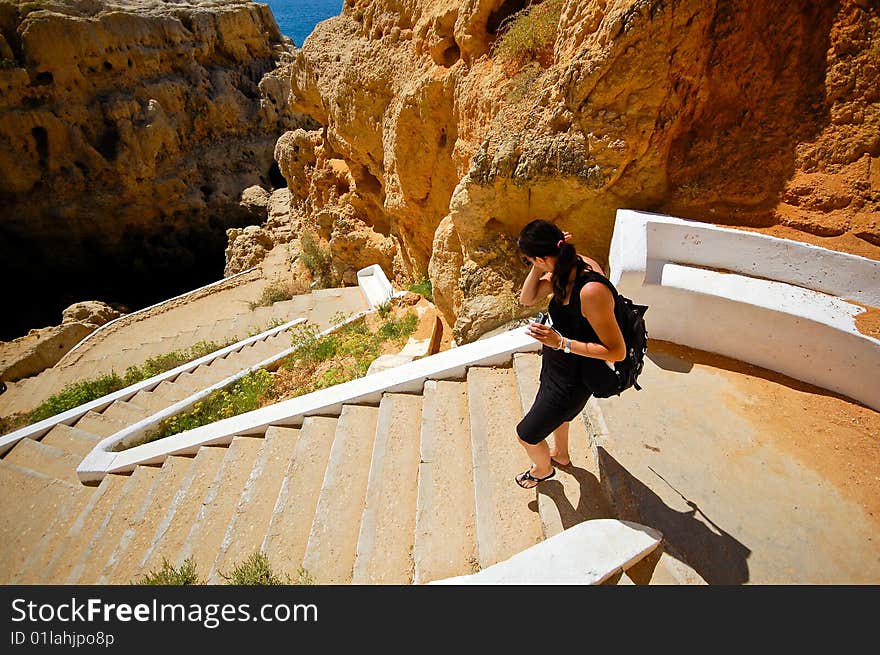 Woman in black take the stairs down to the cave formation at the Algarve coast. Woman in black take the stairs down to the cave formation at the Algarve coast.