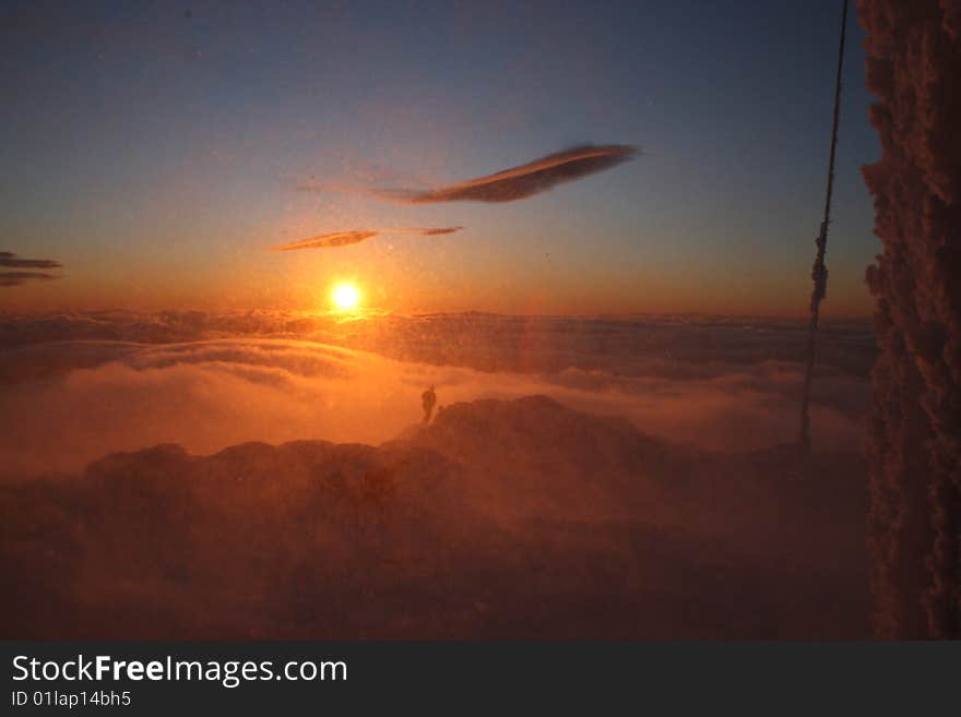 A person alone above the clouds in windy conditions with blowing snow