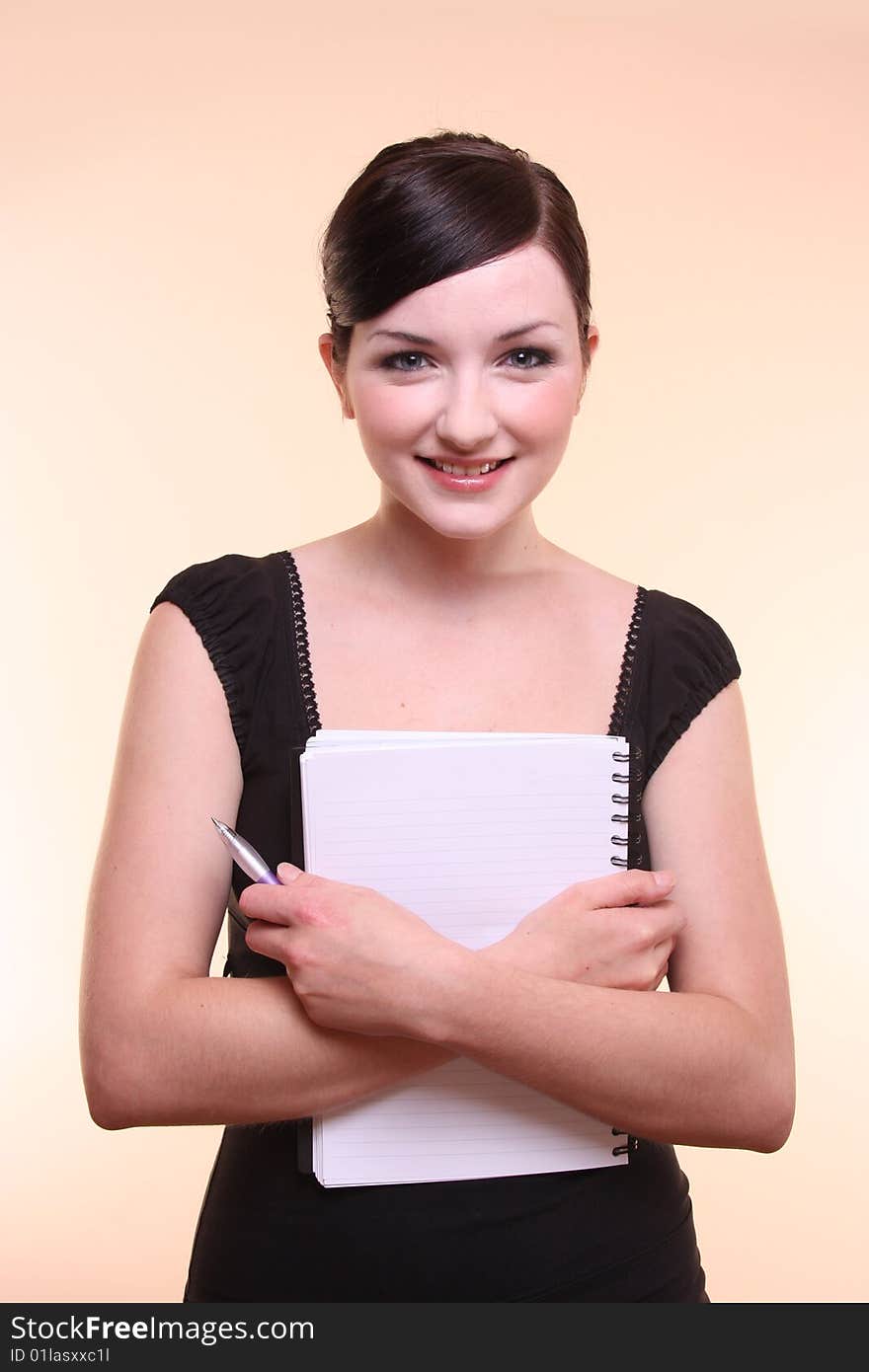 A smiling young professional looking woman holding a notepad in front of a peach background. A smiling young professional looking woman holding a notepad in front of a peach background.