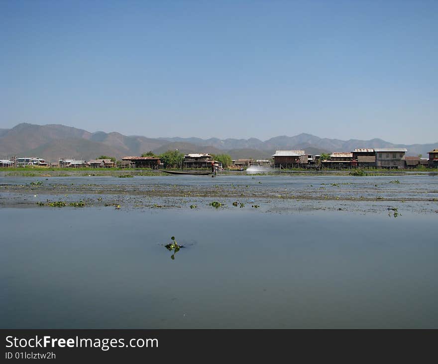 Lakeside village, mountain range and blue sky at the background. Myanmar, Burma.