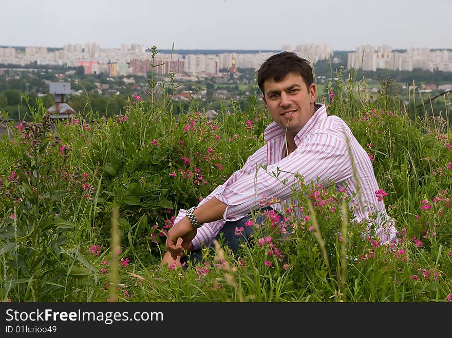 Young man in a pink shirt sitting in the flowering grass. Young man in a pink shirt sitting in the flowering grass