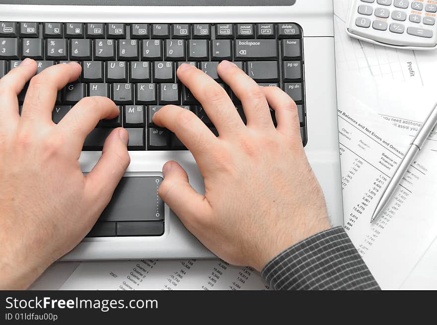 Businessman typing on notebook (laptop) on desk with scientific calculator, elegant silver pen and financial papers