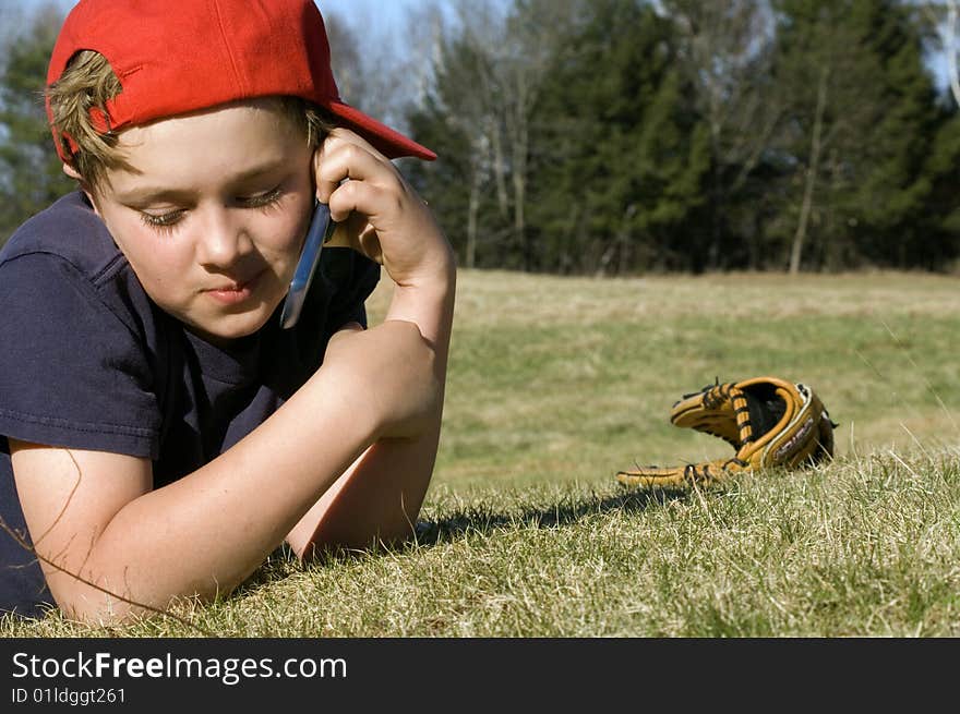 A young boy takes a break from playing baseball to chat on the cellular telephone. A young boy takes a break from playing baseball to chat on the cellular telephone