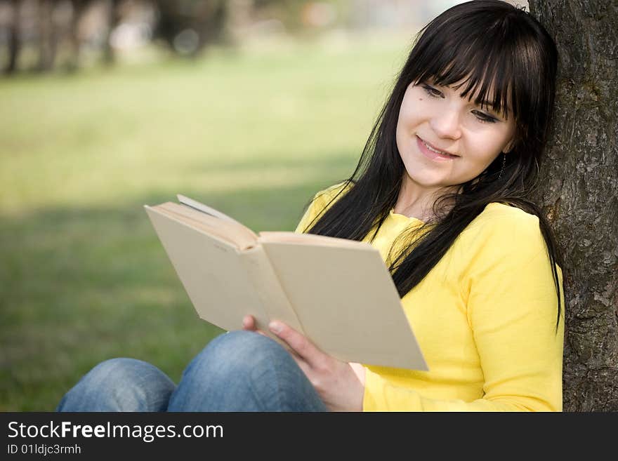 Happy brunette woman reading book in park