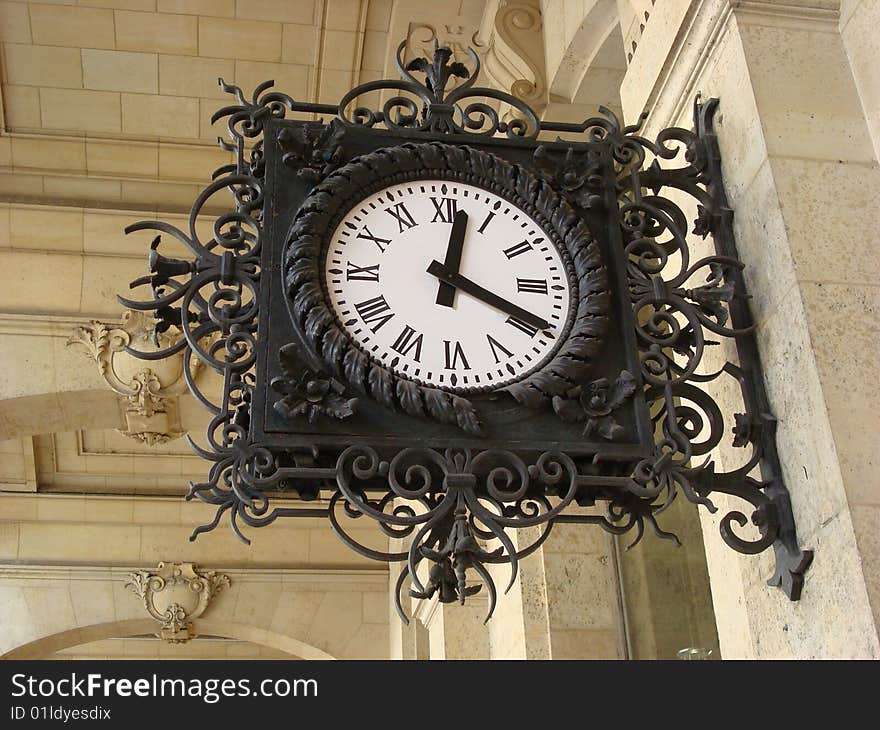 A beautiful old clock hangs in Paris on a street so people passing by can see what time it is. A beautiful old clock hangs in Paris on a street so people passing by can see what time it is