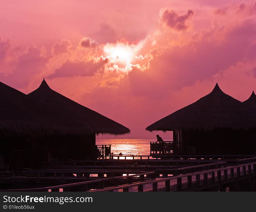 Human silhouette in water bungalow at sunset, abstract vacation background