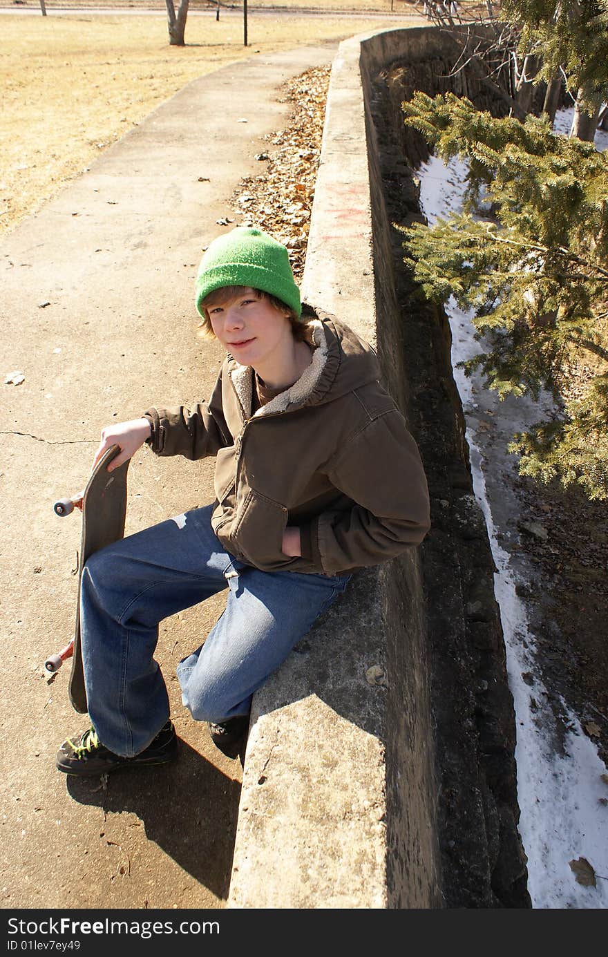 A young teen boy sits on a concrete ledge with his skateboard. A young teen boy sits on a concrete ledge with his skateboard.