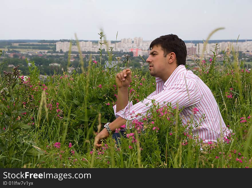 Young man in a pink shirt sitting in the flowering grass. Young man in a pink shirt sitting in the flowering grass