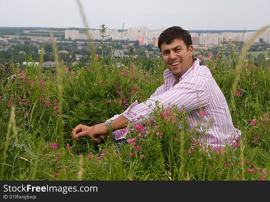 Young man in a pink shirt sitting in the flowering grass. Young man in a pink shirt sitting in the flowering grass