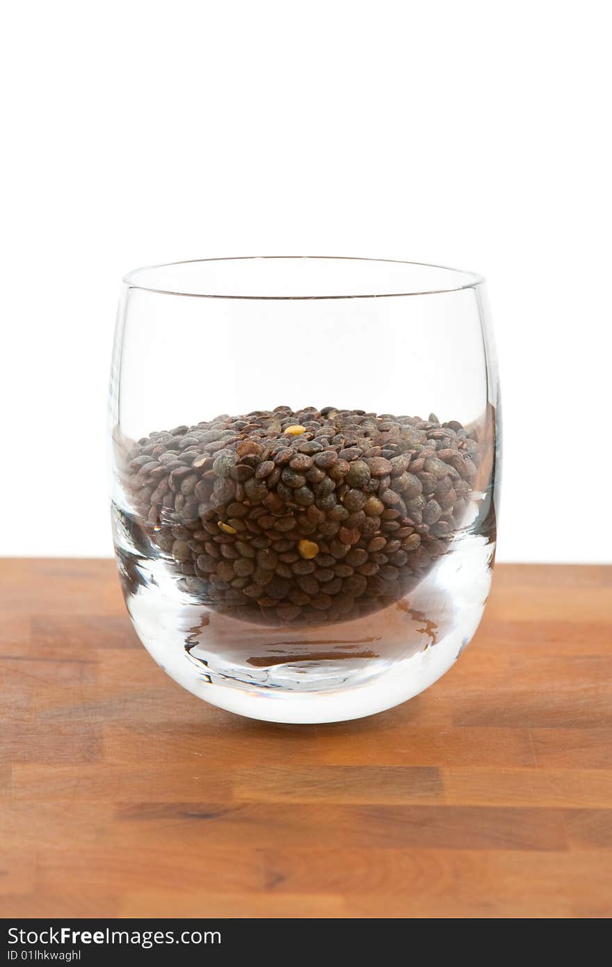 Green lentils in glass on wooden table, white background