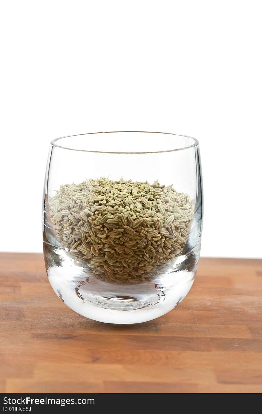 Dried fennel seeds in glass on wooden table, white background