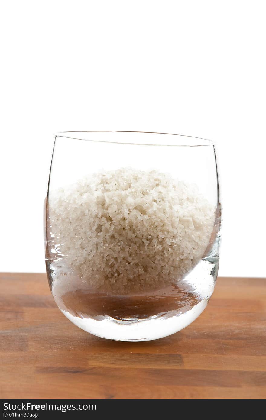 Coarse grey sea salt in glass on wooden table, white background