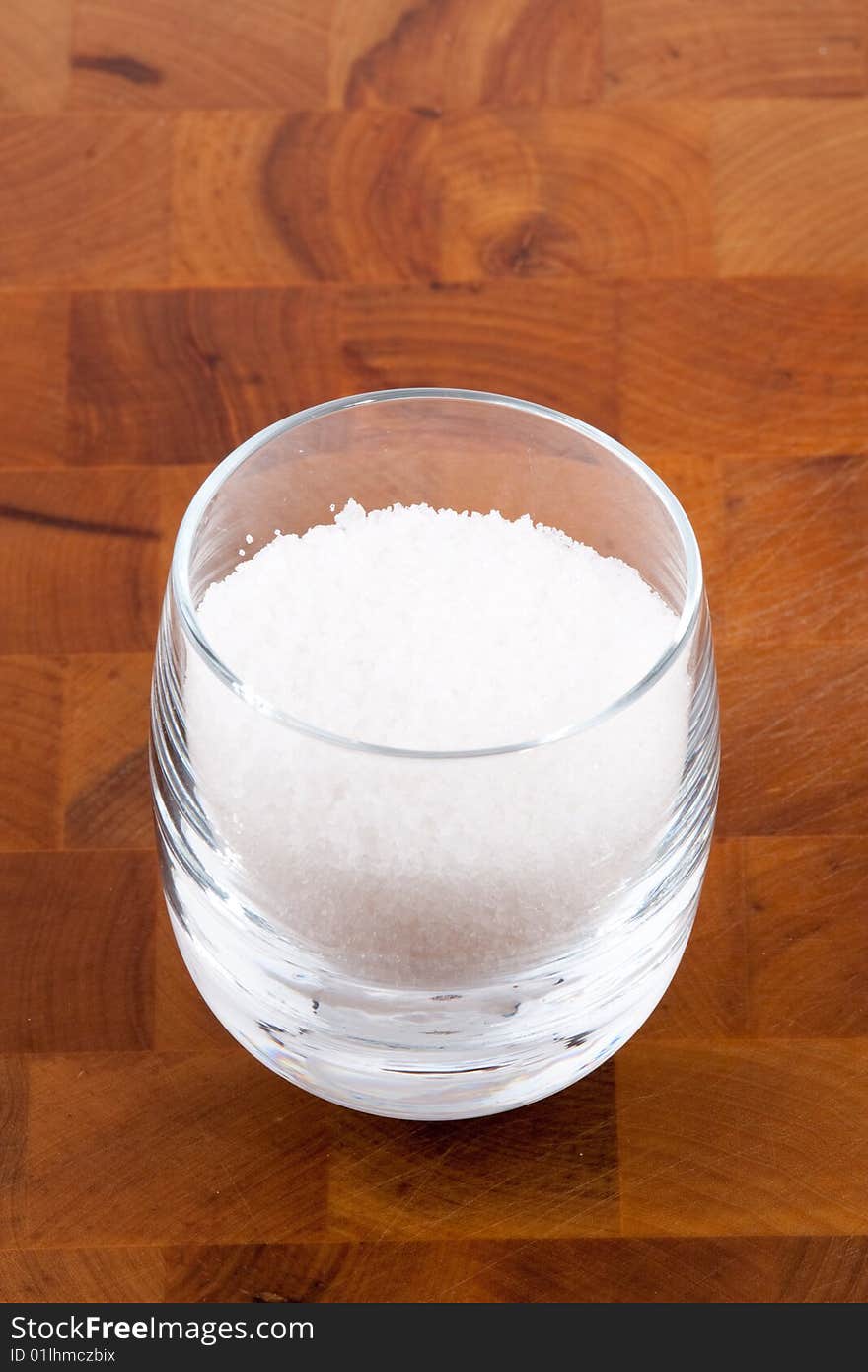 Fleur de sel, white sea salt crystals in glass on wooden table