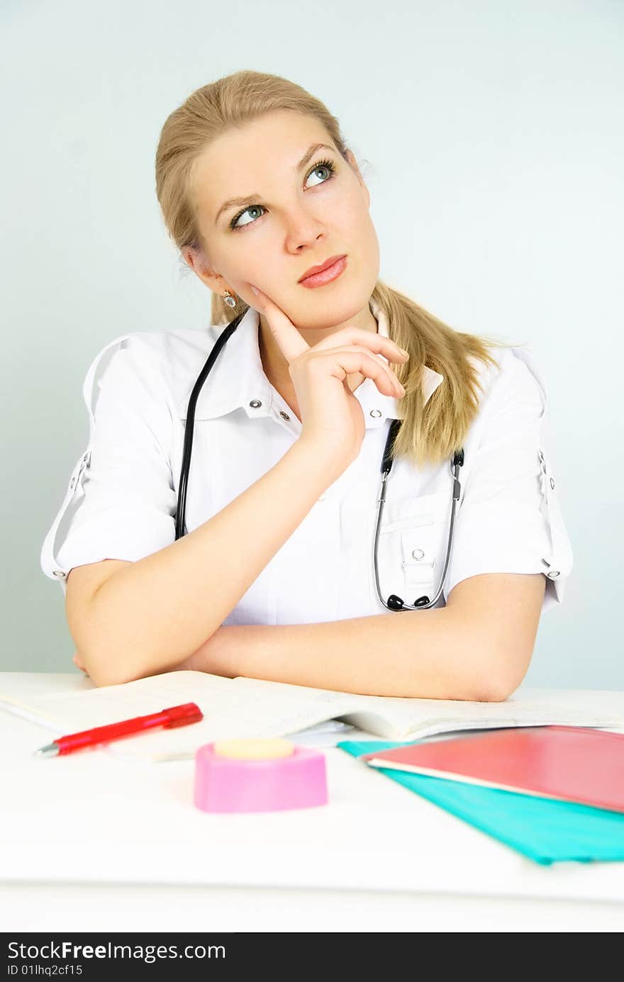 Beautiful thoughtful young doctor sitting by the table in the office. Beautiful thoughtful young doctor sitting by the table in the office