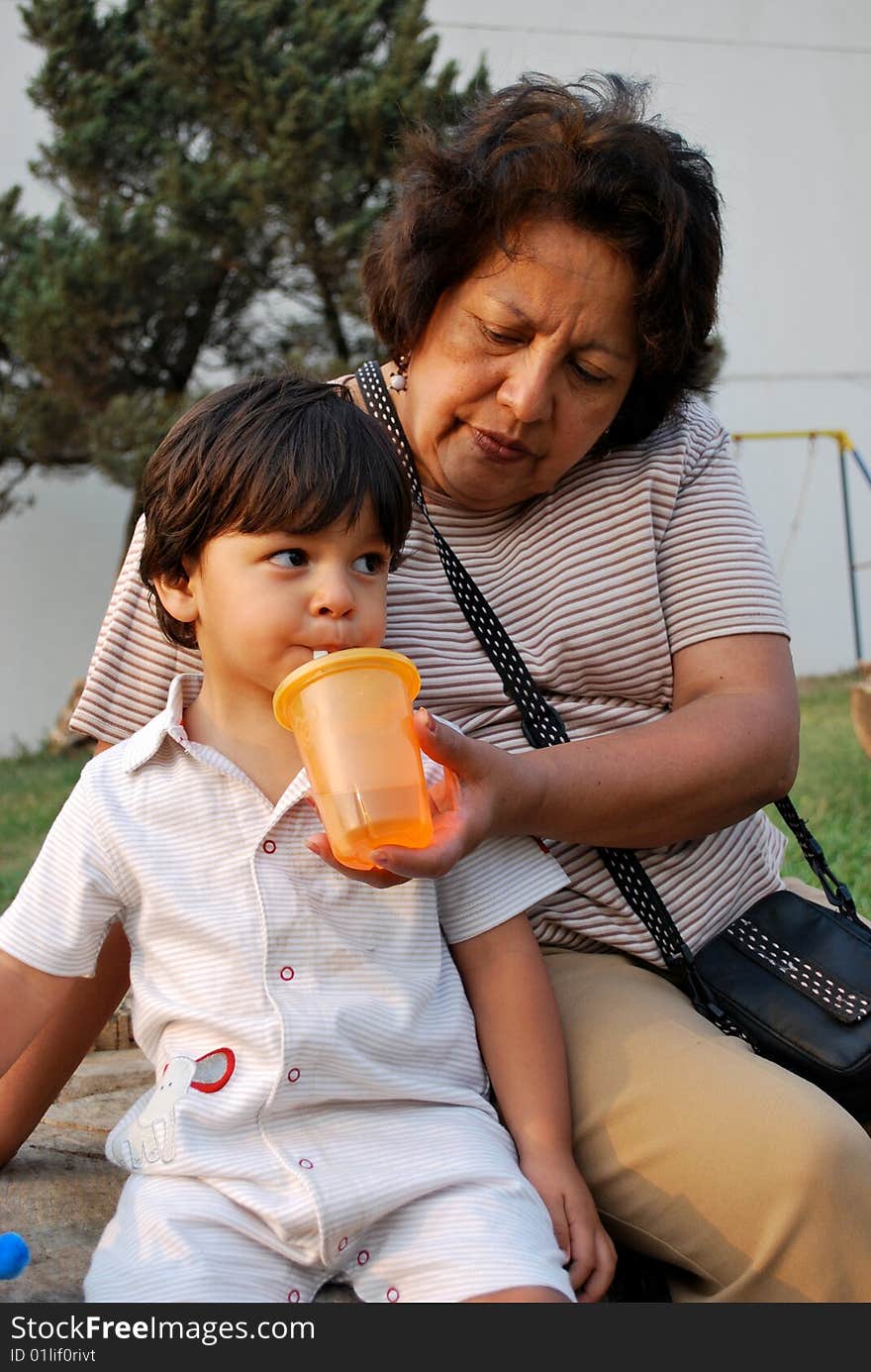 Grandmother feeding her grandson water from a sippy cup.