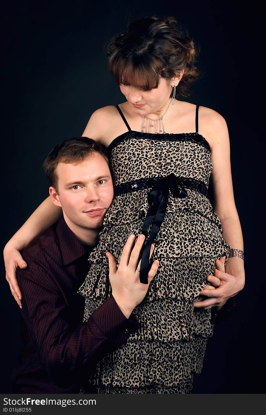 Young beautiful married couple the birth of the second child wait. Dark background. New photos every week