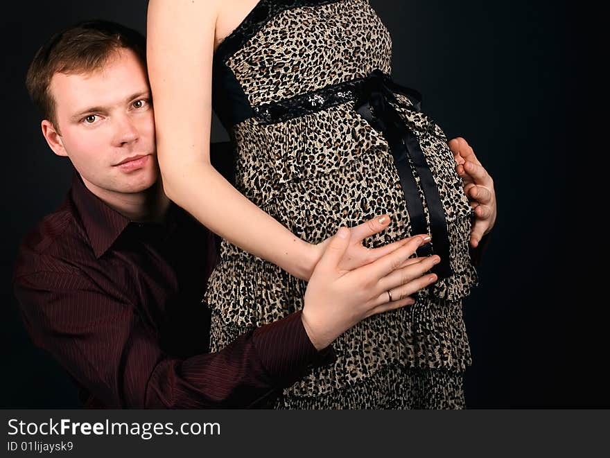 Young beautiful married couple the birth of the second child wait. Dark background. New photos every week