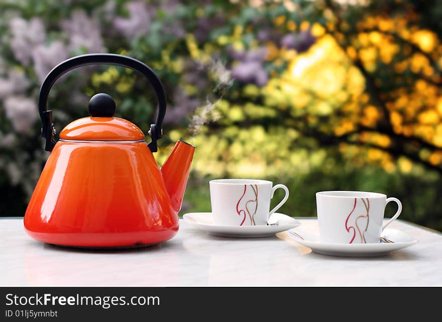 Orange teapot that contains smoking hot tea in front of a blurred background. Orange teapot that contains smoking hot tea in front of a blurred background