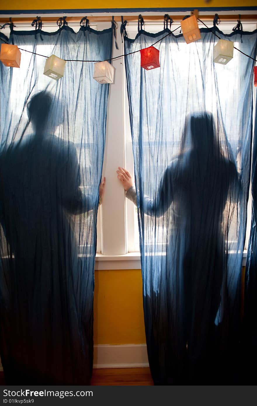 Young couple looking out a window behind blue curtains. Young couple looking out a window behind blue curtains.