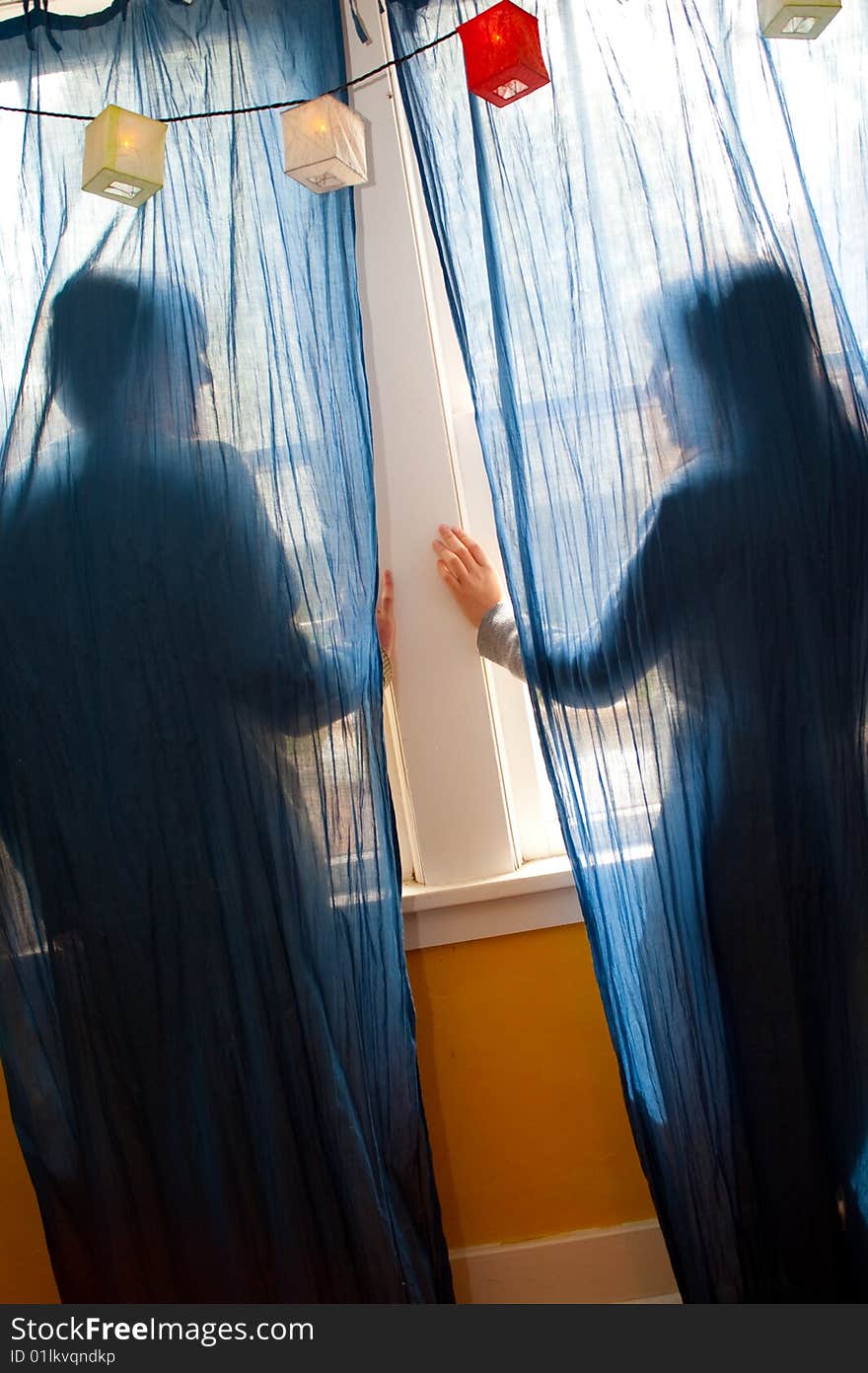 Young couple looking out a window behind blue curtains. Young couple looking out a window behind blue curtains.