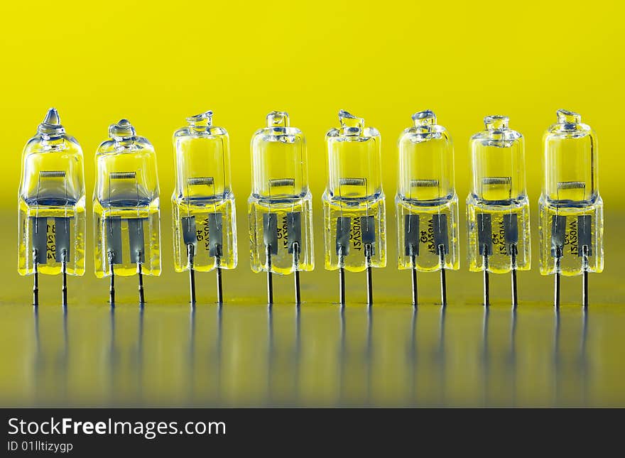 Halogen light bulbs standing in a row on the gradient (yellow-blue) background, there is some reflection in a glass of bulbs. Halogen light bulbs standing in a row on the gradient (yellow-blue) background, there is some reflection in a glass of bulbs