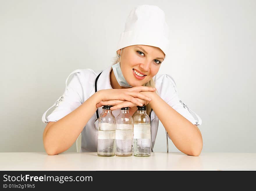 Portrait of a beautiful young doctor with a stethoscope and medications sitting by the table in her office. Portrait of a beautiful young doctor with a stethoscope and medications sitting by the table in her office