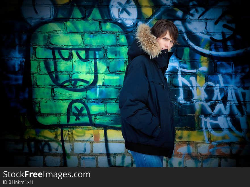 The young guy in a jacket with a hood costs near a wall. The young guy in a jacket with a hood costs near a wall