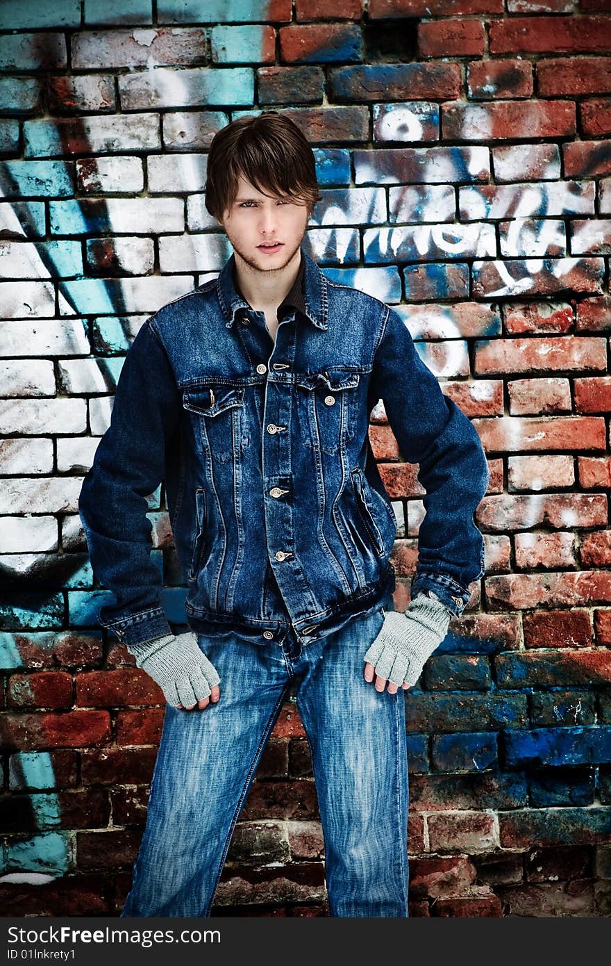 Young guy in jeans costs near to a brick wall. Young guy in jeans costs near to a brick wall