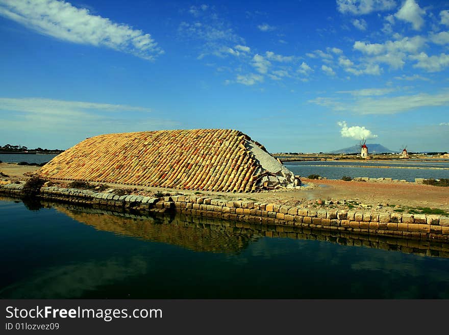 Sea salt production. Sea Salt heaps covered terracotta on the road called The salt road and is remarkable for its numerous mills and rectangular artificial basin the on sea. Trapani, Island of Sicily - Italy. Sea salt production. Sea Salt heaps covered terracotta on the road called The salt road and is remarkable for its numerous mills and rectangular artificial basin the on sea. Trapani, Island of Sicily - Italy