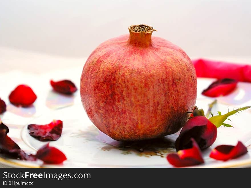 In the center of the plate is a fruit grenades surrounded the petals of red roses. In the center of the plate is a fruit grenades surrounded the petals of red roses.