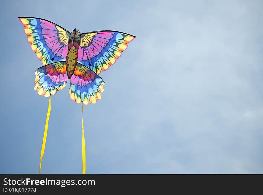 Multi-colored kite flies against a blue sky background. Multi-colored kite flies against a blue sky background