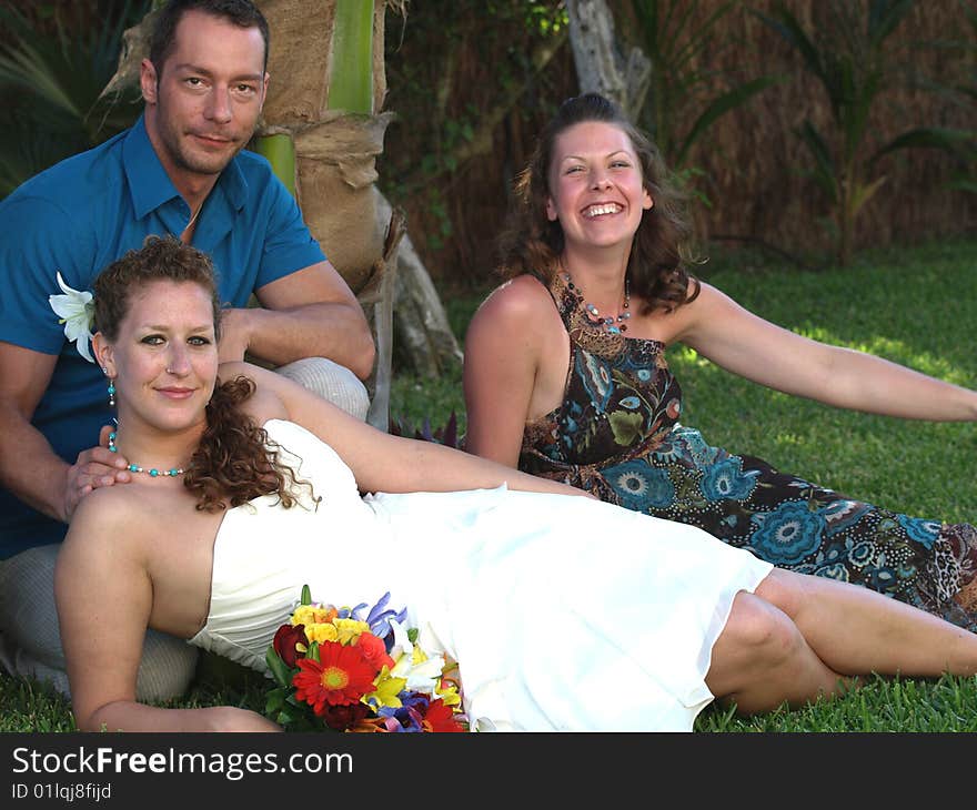 Content bride , groom and bridesmaid,relaxing on the lawn in the shade of a palm tree. Content bride , groom and bridesmaid,relaxing on the lawn in the shade of a palm tree.