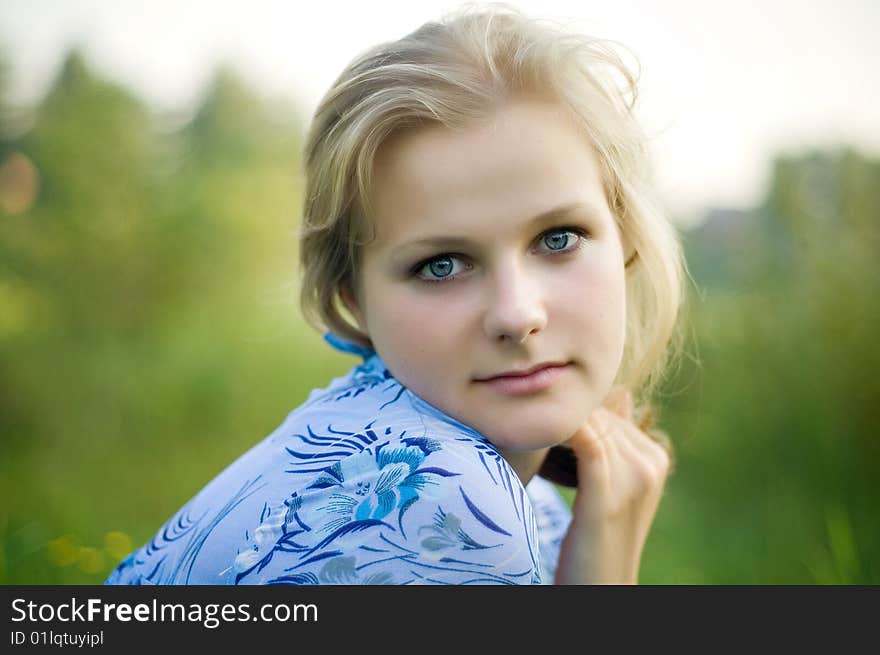 A beautiful blond haired blue eyed model sits amid tall grass