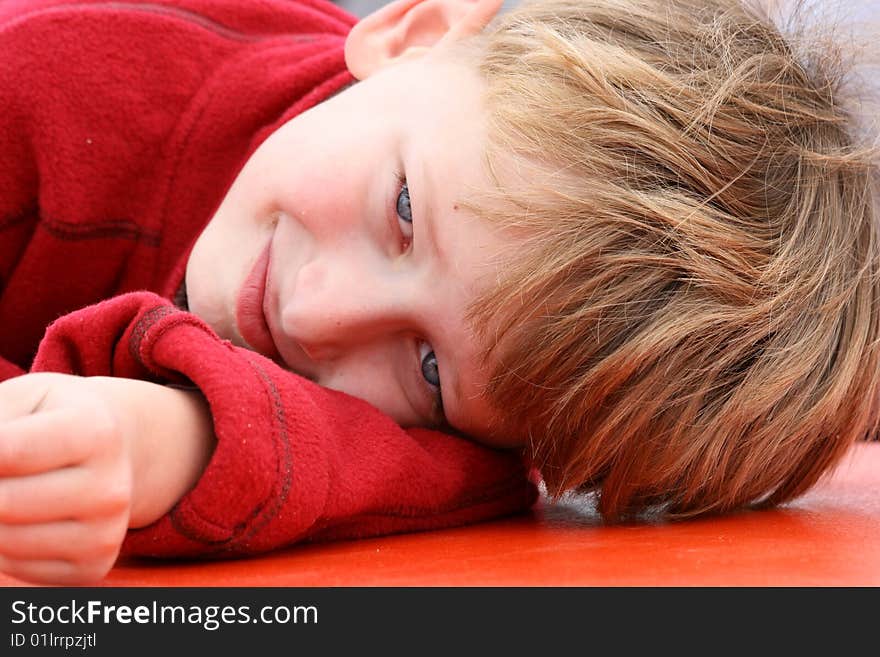 Younf biy in red fleece resting his head on his arm. Younf biy in red fleece resting his head on his arm