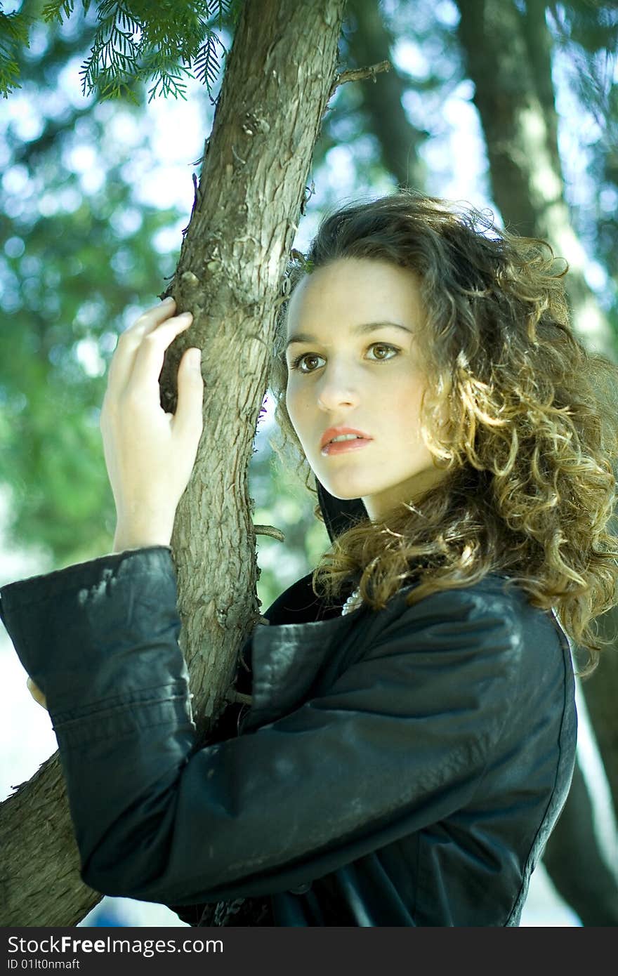 A young girl stands near a tree in a cloak. A young girl stands near a tree in a cloak