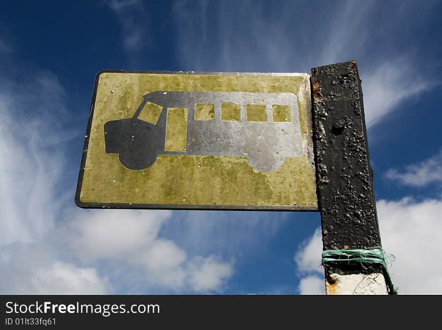 Looking up at a yellow bus stop sign against a blue sky