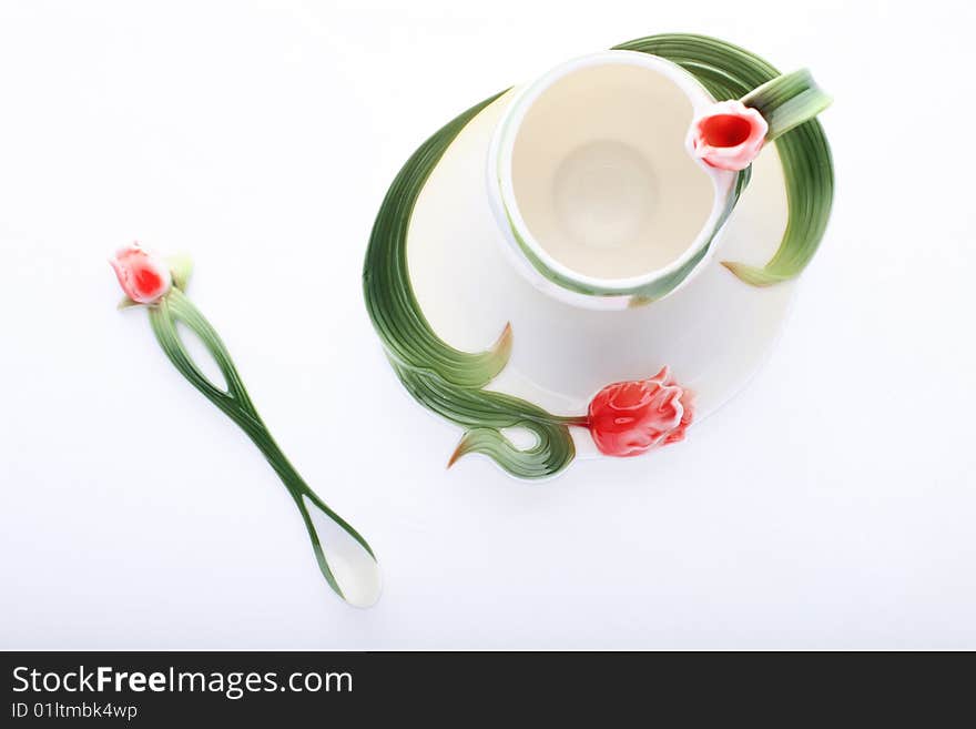 Isolated saucer, cup and spoon decorated with red flower and green color. Isolated saucer, cup and spoon decorated with red flower and green color