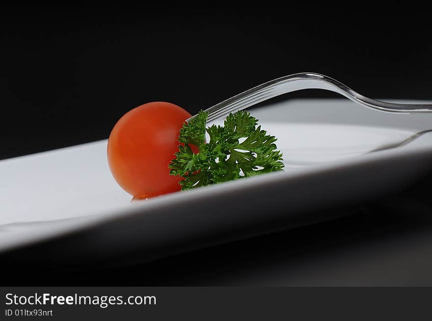 Baby tomato with parsley touched by the fork on white plate. Baby tomato with parsley touched by the fork on white plate